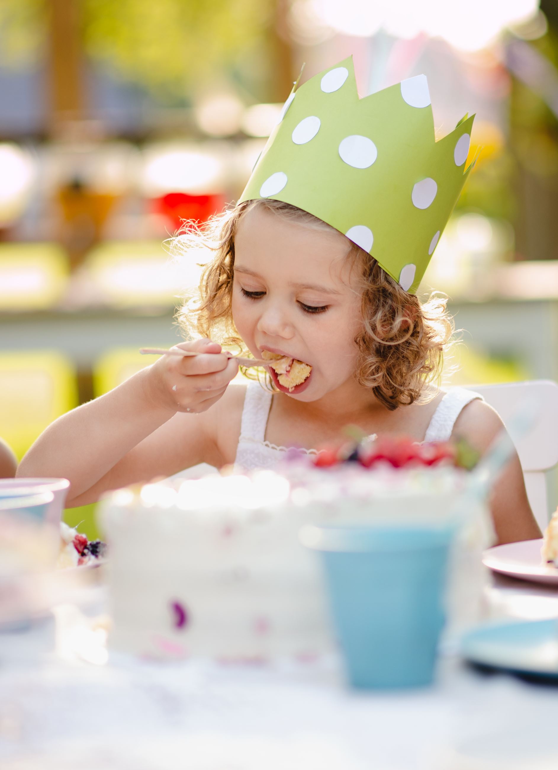 A young girl wearing a birthday crown eats a piece of cake