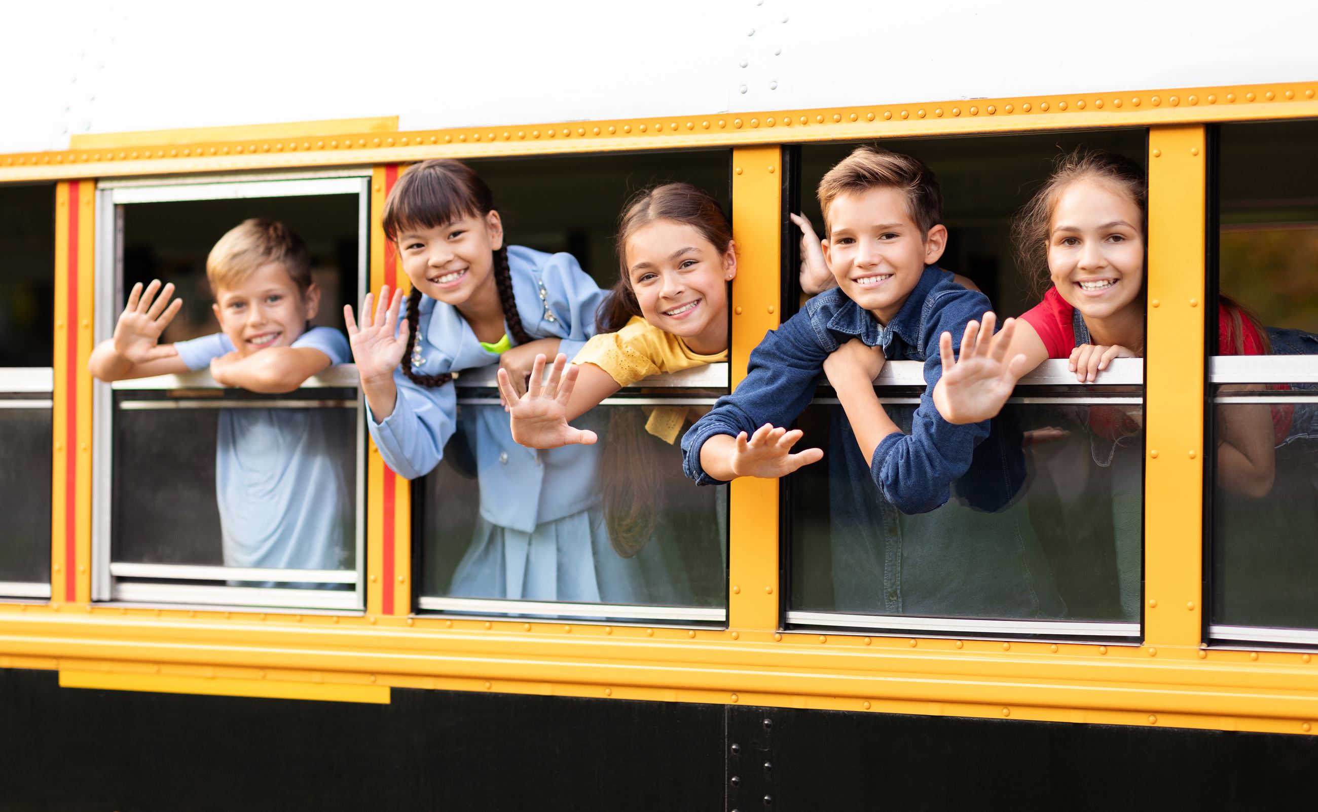 A group of happy kids look out school bus windows and wave